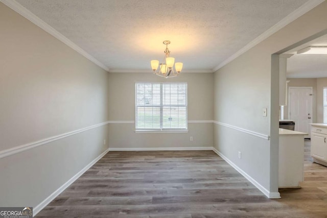 empty room with a chandelier, a textured ceiling, baseboards, and wood finished floors