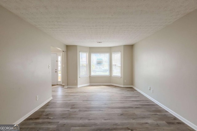 unfurnished room with a textured ceiling, baseboards, and wood finished floors