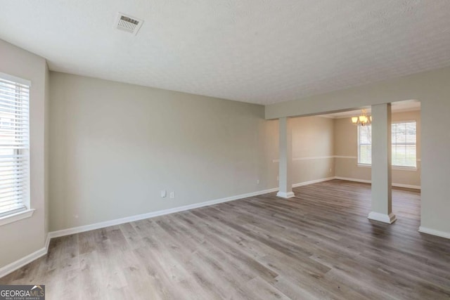 empty room featuring a textured ceiling, wood finished floors, visible vents, and baseboards