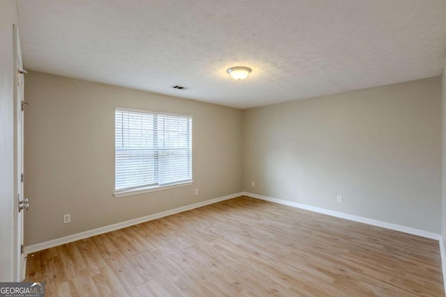 empty room with visible vents, a textured ceiling, light wood-style flooring, and baseboards