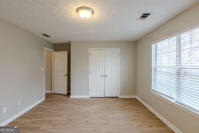 unfurnished bedroom featuring light wood-type flooring, baseboards, visible vents, and a closet