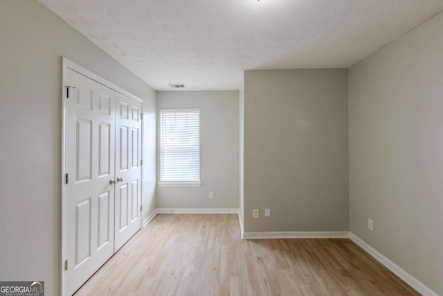 unfurnished bedroom featuring a textured ceiling, a closet, light wood-type flooring, and baseboards