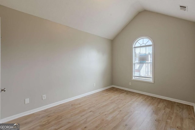 empty room featuring lofted ceiling, light wood finished floors, baseboards, and visible vents