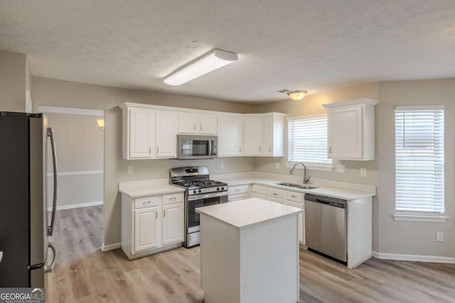 kitchen featuring light wood finished floors, stainless steel appliances, light countertops, white cabinetry, and a sink