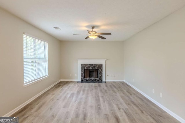 unfurnished living room featuring ceiling fan, visible vents, a high end fireplace, baseboards, and light wood finished floors