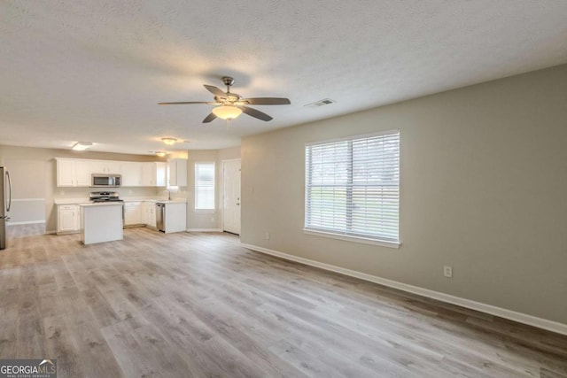 unfurnished living room with visible vents, a ceiling fan, a textured ceiling, light wood-type flooring, and baseboards