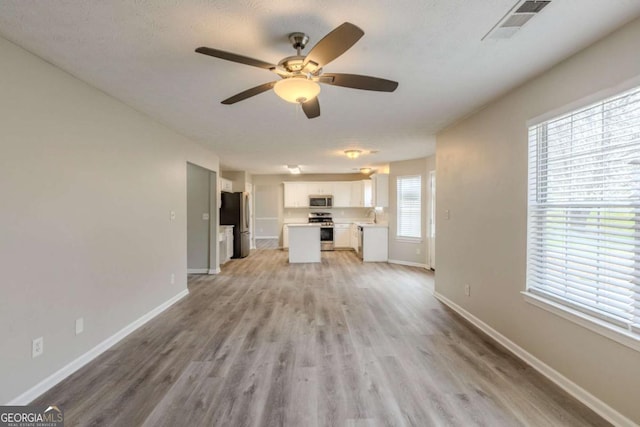 unfurnished living room with ceiling fan, light wood finished floors, visible vents, and baseboards