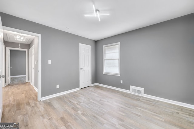 unfurnished bedroom featuring light wood-type flooring, attic access, visible vents, and baseboards