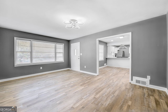 unfurnished living room with baseboards, visible vents, and light wood-style floors