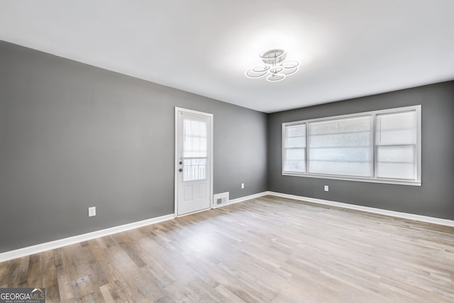 spare room with wood finished floors, visible vents, and baseboards