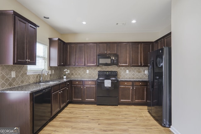 kitchen with visible vents, light wood-style flooring, a sink, dark stone countertops, and black appliances