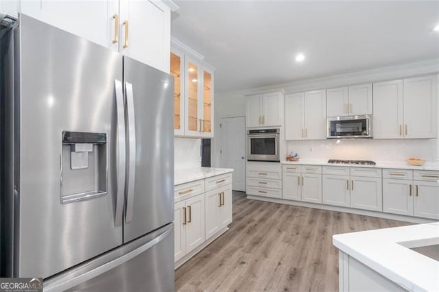 kitchen with light wood finished floors, appliances with stainless steel finishes, decorative backsplash, and white cabinetry