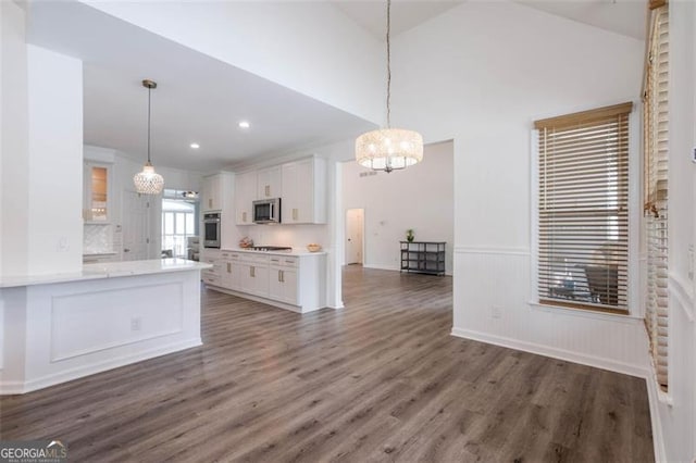 kitchen featuring a wainscoted wall, dark wood finished floors, hanging light fixtures, appliances with stainless steel finishes, and white cabinets