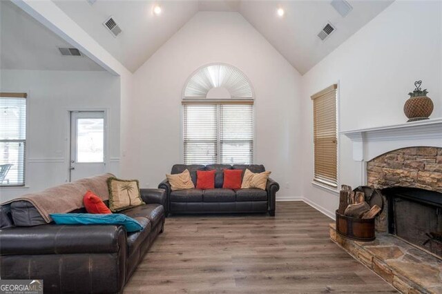 living area featuring high vaulted ceiling, visible vents, wood finished floors, and a stone fireplace