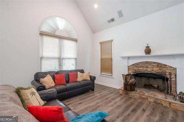 living room with high vaulted ceiling, visible vents, wood finished floors, and a stone fireplace