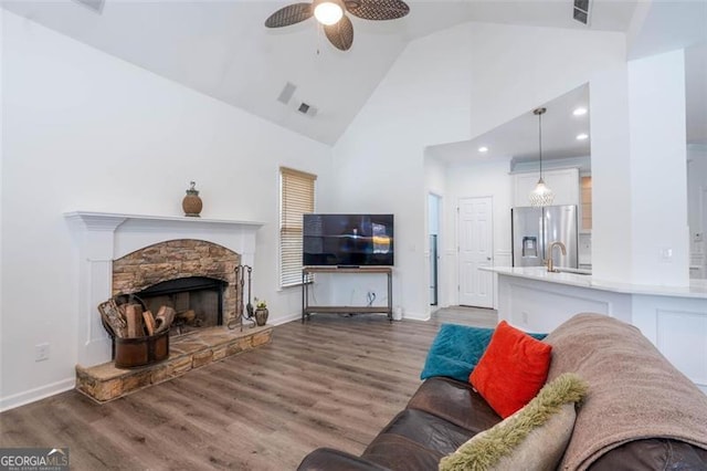 living room with visible vents, a ceiling fan, wood finished floors, a stone fireplace, and high vaulted ceiling