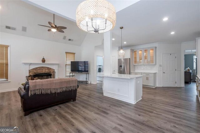 kitchen featuring white cabinetry, glass insert cabinets, a fireplace, stainless steel fridge, and ceiling fan with notable chandelier
