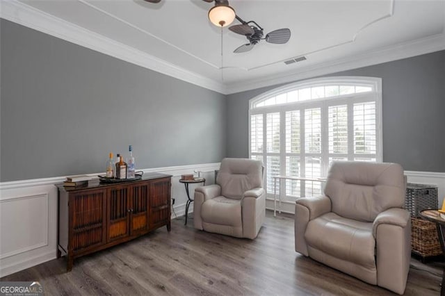 living area with crown molding, visible vents, wainscoting, ceiling fan, and wood finished floors