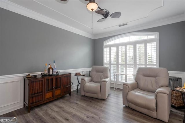living area with wood finished floors, visible vents, a ceiling fan, and wainscoting