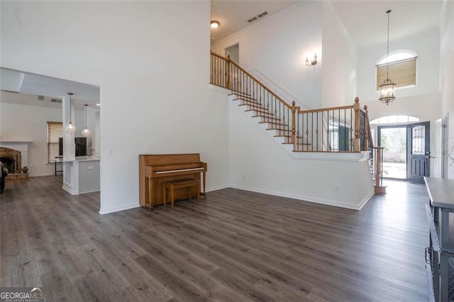 unfurnished living room with a towering ceiling, visible vents, stairway, and dark wood finished floors