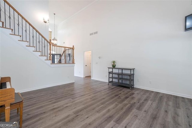 unfurnished living room with wood finished floors, a towering ceiling, visible vents, baseboards, and stairway