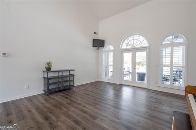 unfurnished living room featuring wood finished floors, a healthy amount of sunlight, french doors, and a towering ceiling