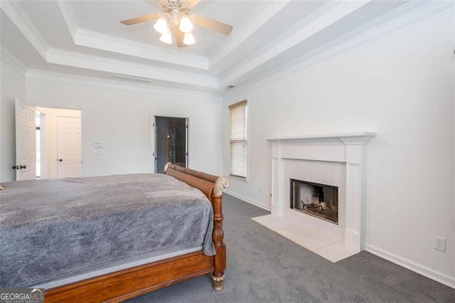 bedroom featuring a raised ceiling, a ceiling fan, a tiled fireplace, carpet, and crown molding