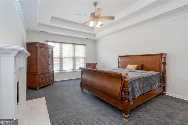 bedroom featuring baseboards, a fireplace with flush hearth, a tray ceiling, crown molding, and carpet flooring