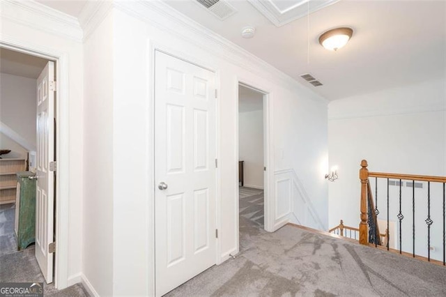 hallway with an upstairs landing, visible vents, ornamental molding, and carpet floors