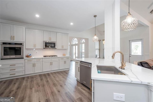 kitchen featuring stainless steel appliances, tasteful backsplash, hanging light fixtures, light wood-style flooring, and a sink