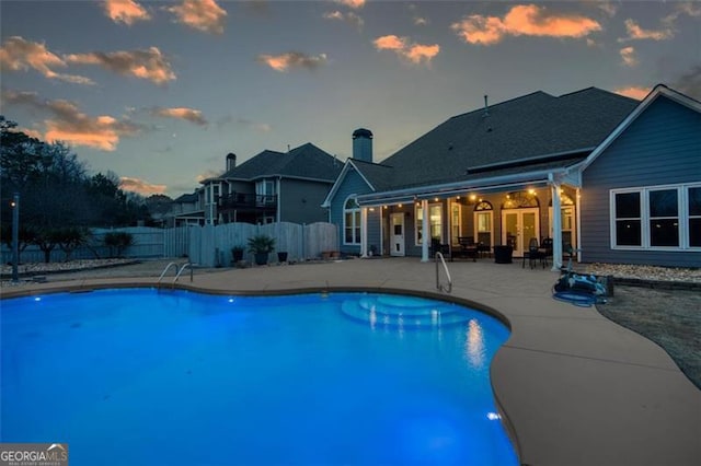 pool at dusk with a patio, a fenced in pool, and fence