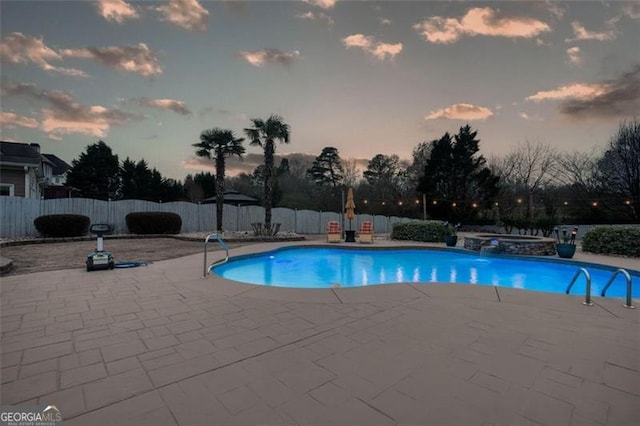 pool at dusk with a fenced backyard, a pool with connected hot tub, and a patio