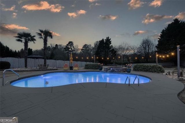 pool at dusk featuring a patio area, a fenced backyard, and a pool with connected hot tub