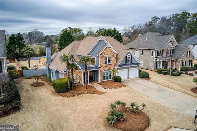 traditional-style home with concrete driveway, stone siding, a chimney, fence, and a garage