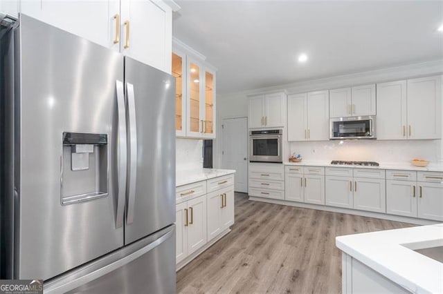 kitchen featuring stainless steel appliances, white cabinetry, light countertops, backsplash, and glass insert cabinets