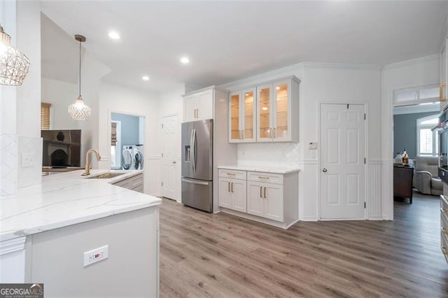 kitchen featuring light stone counters, stainless steel fridge, a sink, light wood-type flooring, and washer and clothes dryer