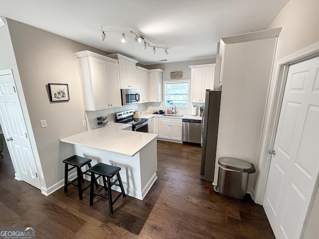 kitchen with dark wood finished floors, appliances with stainless steel finishes, a peninsula, white cabinetry, and a sink