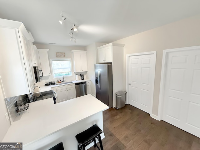 kitchen with appliances with stainless steel finishes, dark wood-type flooring, a peninsula, light countertops, and a sink