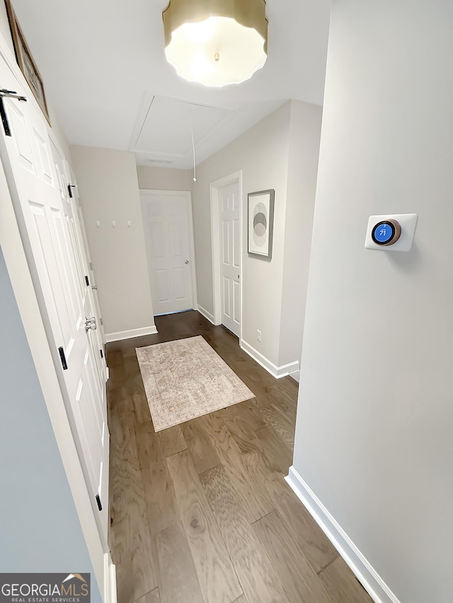 hall with attic access, baseboards, and dark wood-style flooring