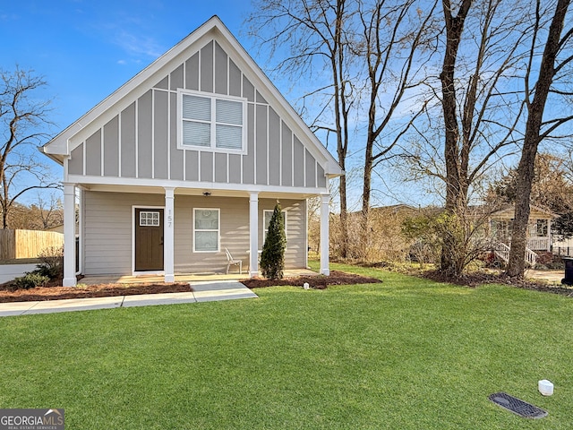 view of front of house with board and batten siding, covered porch, fence, and a front lawn