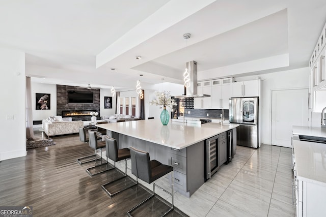 kitchen with beverage cooler, a tray ceiling, a fireplace, smart refrigerator, and island range hood