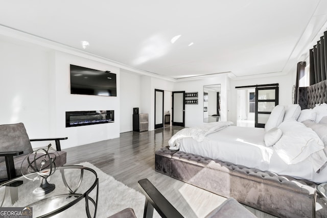 bedroom with wood finished floors, a glass covered fireplace, and crown molding