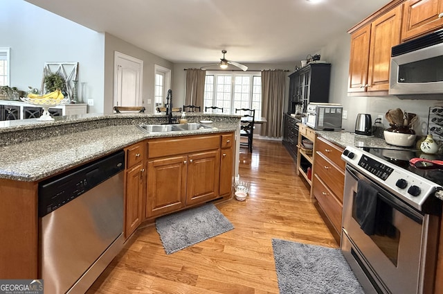 kitchen with stainless steel appliances, a sink, light wood-style floors, brown cabinets, and light stone countertops