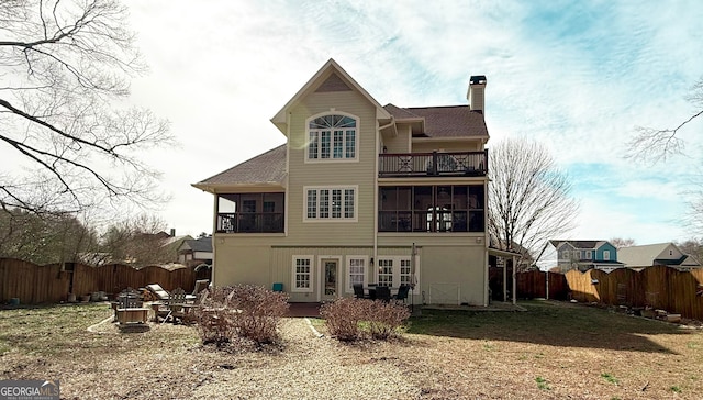 back of house with a sunroom, a chimney, a fenced backyard, and a balcony