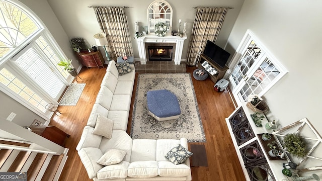 living room with wood finished floors, a tile fireplace, a high ceiling, and baseboards