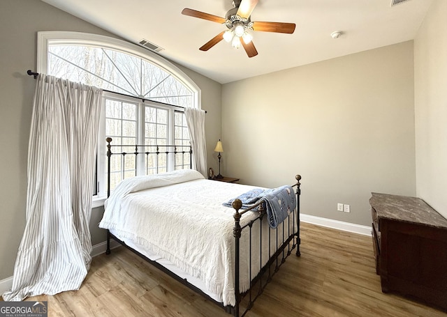 bedroom featuring baseboards, multiple windows, visible vents, and wood finished floors