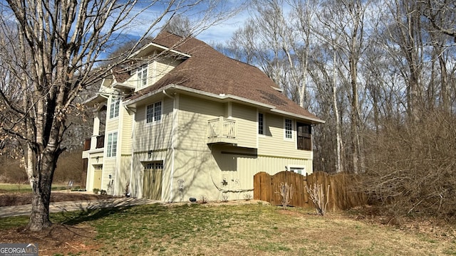 view of property exterior with a balcony, a shingled roof, and fence