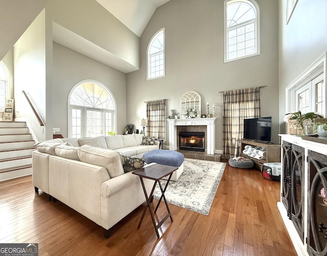 living area featuring stairway, wood-type flooring, a tile fireplace, and a healthy amount of sunlight