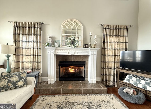 living area featuring dark wood-type flooring, a tiled fireplace, and baseboards