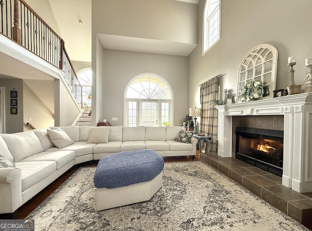 living room with stairway, a tiled fireplace, and a towering ceiling